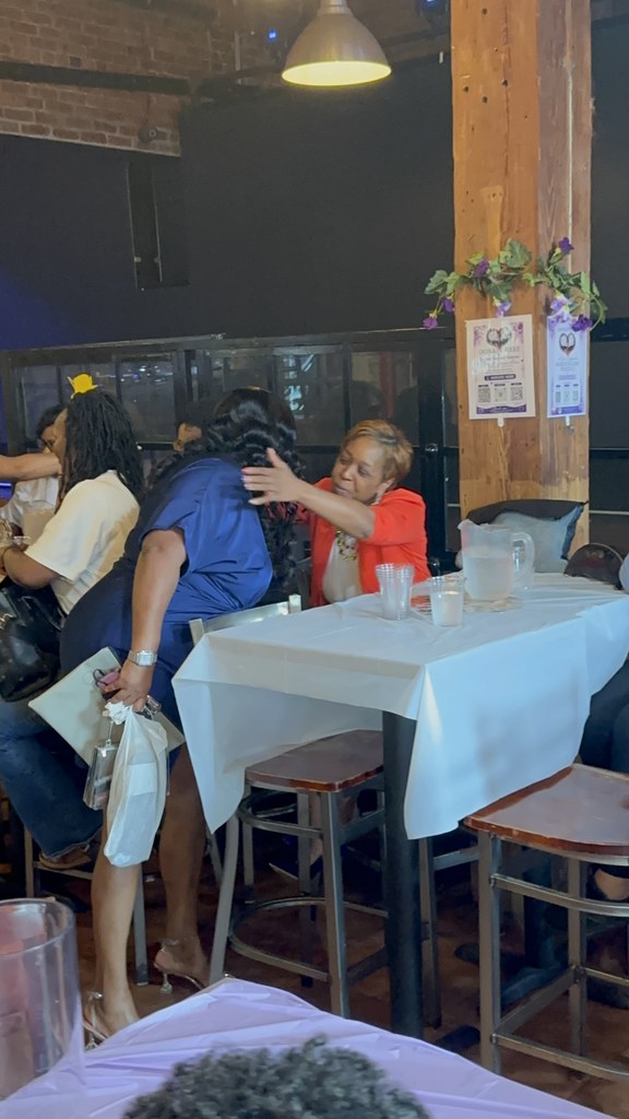 The founder embracing a guest at her table