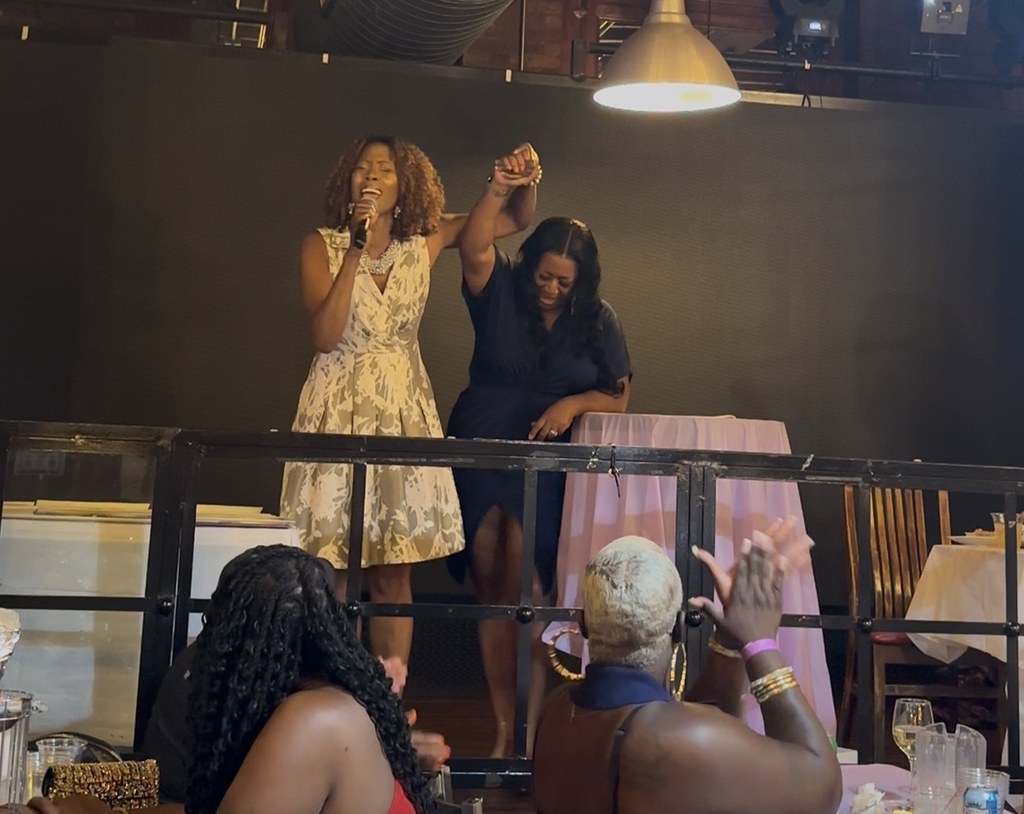 A vocalist performing as the founder lifts her hand beside her