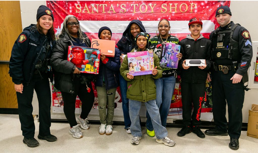 Families and local officers with gifts in front of the Santa's Toy Shop banner