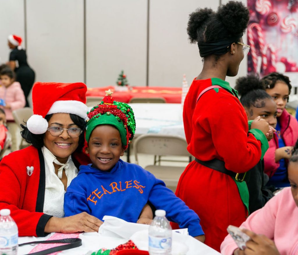 Family in elf and holiday outfits posing with Santa at the toy drive