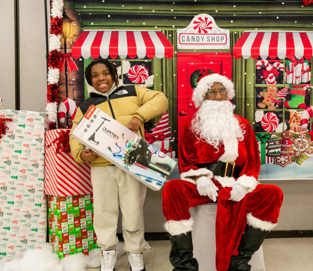A young guest receiving a scooter beside Santa